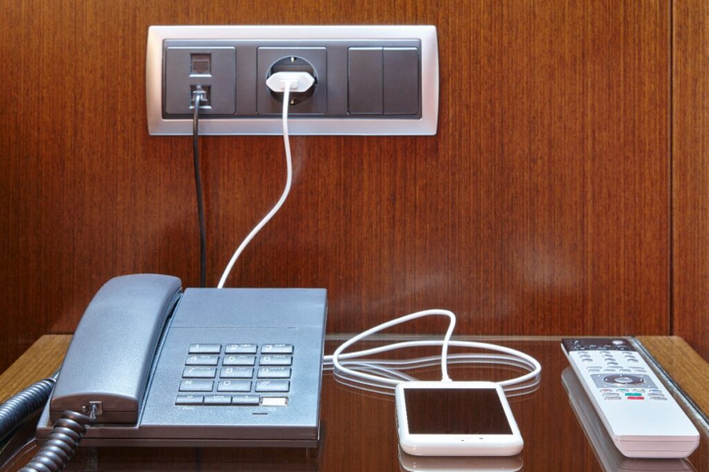 Un téléphone portable en charge déposée sur table avec un téléphone fixe et une télécommande