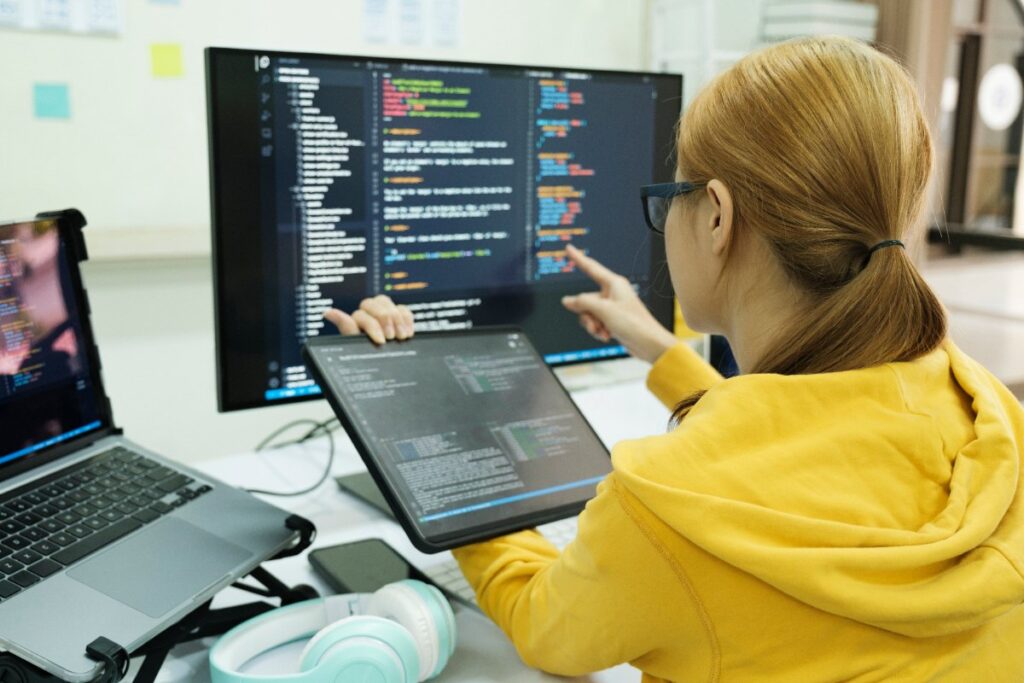 Une femme travaillant sur une tablette et des ordinateurs en lisant des codes